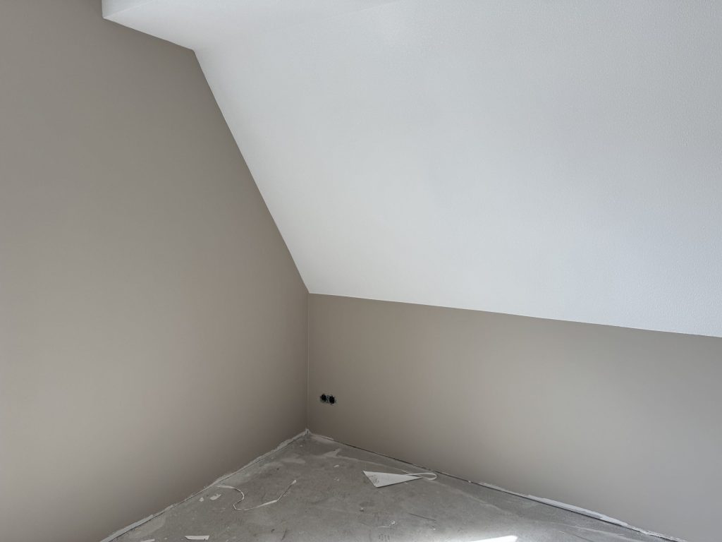 Zolderkamer met schuin plafond, grijze wanden en een afgedekte vloer