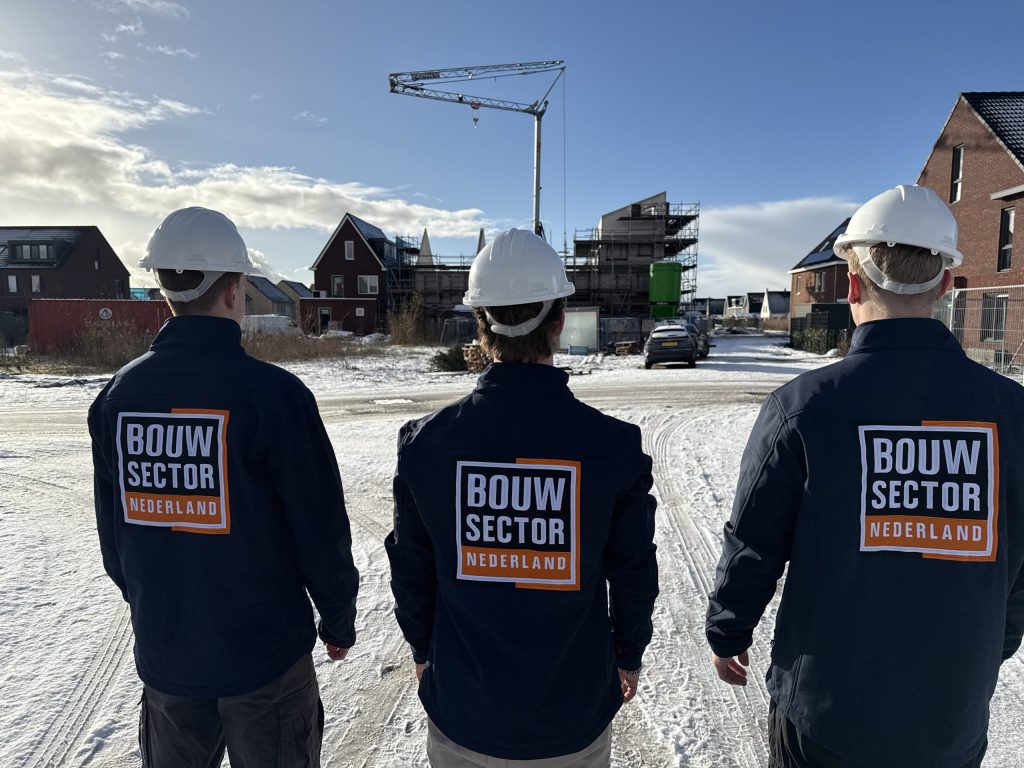Drie vakmensen van Bouwsector Nederland met witte helm kijken naar een rij nieuwe woningen